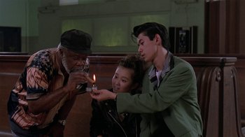 Movie still from “Mystery Train” (1989), directed by Jim Jarmusch – A group of people lighting a candle in a church; Medium shot, Low angle