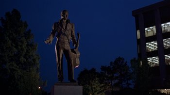 Movie still from “Mystery Train” (1989), directed by Jim Jarmusch – A statue of a man holding a guitar stands in front of trees at night; Wide shot, Low angle