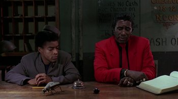 Movie still from “Mystery Train” (1989), directed by Jim Jarmusch – Two men sitting at a wooden table in front of a clock; Medium shot, Low angle