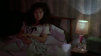 Movie still from “Mystery Train” (1989), directed by Jim Jarmusch – A woman sitting in a bed with a lamp on the side of the bed; Medium shot, High angle