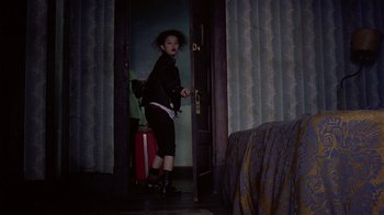 Movie still from “Mystery Train” (1989), directed by Jim Jarmusch – A woman with a red suitcase standing in a doorway; Wide shot, High angle