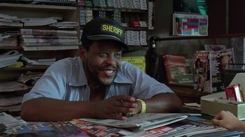Movie still from “Mystery Train” (1989), directed by Jim Jarmusch – A man sitting at a table in front of a stack of magazines; Close Up shot, Low angle