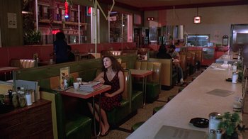Movie still from “Mystery Train” (1989), directed by Jim Jarmusch – A woman sitting at a booth in a restaurant; Wide shot, High angle