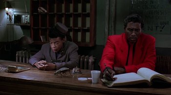 Movie still from “Mystery Train” (1989), directed by Jim Jarmusch – Two men sitting at a wooden table in a room; Medium shot, Low angle