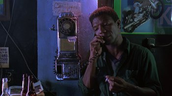 Movie still from “Mystery Train” (1989), directed by Jim Jarmusch – A man talking on a phone in front of an old phone booth; Close Up shot, High angle