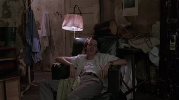 Movie still from “Mystery Train” (1989), directed by Jim Jarmusch – A man sitting in a chair in a living room; Medium shot, Low angle