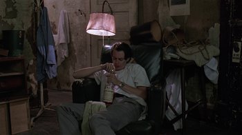 Movie still from “Mystery Train” (1989), directed by Jim Jarmusch – A man sitting in a chair with a bottle of alcohol; Medium shot, High angle