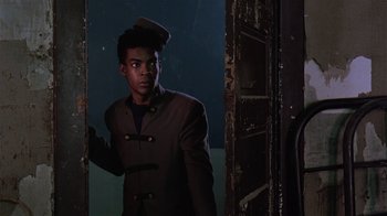 Movie still from “Mystery Train” (1989), directed by Jim Jarmusch – A man in a brown jacket standing next to a door; Medium shot, Low angle