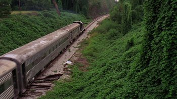 Movie still from “Mystery Train” (1989), directed by Jim Jarmusch – A train traveling down train tracks next to a lush green forest; Extreme Wide shot, High angle