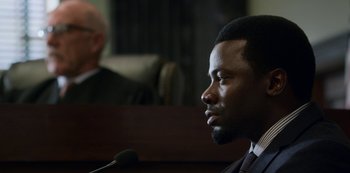 Movie still from “13 Reasons Why” (2017), created by Brian Yorkey – A man in a suit and tie in a court room; Close Up shot, Over the shoulder angle