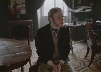 Movie still from “A Few Days from the Life of I.I. Oblomov” (1980), directed by Nikita Mikhalkov – A man sitting in a chair in front of a table; Medium shot, Over the shoulder angle