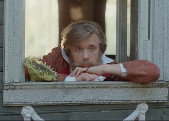 Movie still from “A Few Days from the Life of I.I. Oblomov” (1980), directed by Nikita Mikhalkov – A man leaning up against a window sill with a lizard on his lap; Close Up shot, Low angle