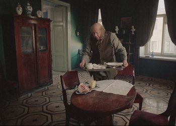 Movie still from “A Few Days from the Life of I.I. Oblomov” (1980), directed by Nikita Mikhalkov – An old man sitting at a table with plates of food; Wide shot, High angle