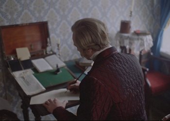 Movie still from “A Few Days from the Life of I.I. Oblomov” (1980), directed by Nikita Mikhalkov – A man is reading a book at a desk; Medium shot, High angle