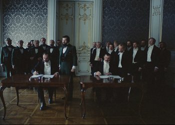 Movie still from “A Few Days from the Life of I.I. Oblomov” (1980), directed by Nikita Mikhalkov – A group of men sitting at a table in front of a wall; Wide shot, High angle