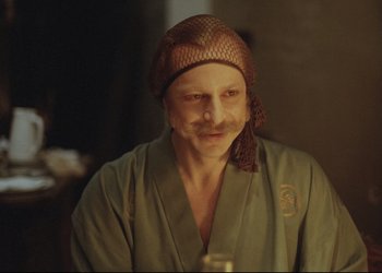 Movie still from “A Few Days from the Life of I.I. Oblomov” (1980), directed by Nikita Mikhalkov – A man with a beard wearing a hat and holding a glass; Close Up shot, Over the shoulder angle