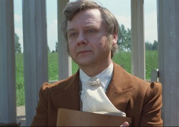 Movie still from “A Few Days from the Life of I.I. Oblomov” (1980), directed by Nikita Mikhalkov – A man in a brown suit holding a book in his hands; Close Up shot, Low angle