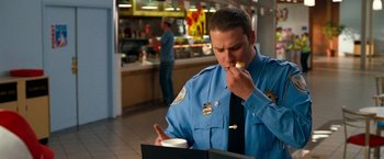Movie still from “Observe and Report” (2009), directed by Jody Hill – A police officer eating a donut while looking at a menu in a restaurant; Medium shot, Over the shoulder angle