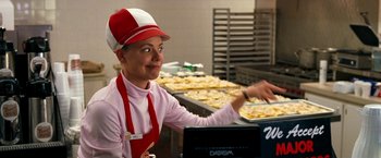 Movie still from “Observe and Report” (2009), directed by Jody Hill – A woman wearing a red hat and a red apron is preparing pizzas in a kitchen; Medium shot, Over the shoulder angle