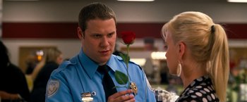 Movie still from “Observe and Report” (2009), directed by Jody Hill – A police officer holding a red rose in front of a woman; Close Up shot, Over the shoulder angle