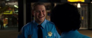 Movie still from “Observe and Report” (2009), directed by Jody Hill – A police officer smiling at the camera while talking to another person; Close Up shot, Over the shoulder angle