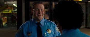 Movie still from “Observe and Report” (2009), directed by Jody Hill – A police officer smiling at the camera while talking to another person; Close Up shot, Over the shoulder angle