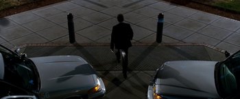 Movie still from “Observe and Report” (2009), directed by Jody Hill – A man in a black suit walking on a sidewalk near parked cars at night; Wide shot, High angle