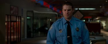 Movie still from “Observe and Report” (2009), directed by Jody Hill – A man in a police uniform standing next to a building; Close Up shot, Over the shoulder angle