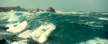 Movie still from “Oceans” (2009), directed by Jacques Cluzaud – A person on a surfboard riding a wave in the ocean; Extreme Wide shot, High angle