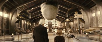 Movie still from “Oceans” (2009), directed by Jacques Cluzaud – A man and a boy looking at an airplane in a hangar; Wide shot, Low angle