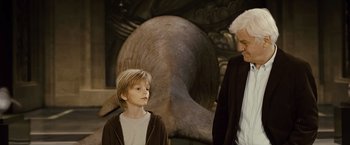 Movie still from “Oceans” (2009), directed by Jacques Cluzaud – A man and a boy standing next to each other in front of an elephant statue; Medium shot, Over the shoulder angle