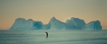 Movie still from “Oceans” (2009), directed by Jacques Cluzaud – A penguin is walking on the ice in the middle of the day; Extreme Wide shot, Low angle