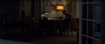 Movie still from “October Sky” (1999), directed by Joe Johnston – A man sitting at a table in front of a laptop computer; Wide shot, High angle