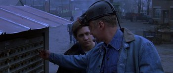 Movie still from “October Sky” (1999), directed by Joe Johnston – A man wearing a hard hat talking to another man; Medium shot, Over the shoulder angle