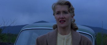 Movie still from “October Sky” (1999), directed by Joe Johnston – A woman in a brown jacket standing in front of a car; Close Up shot, Low angle