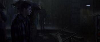 Movie still from “October Sky” (1999), directed by Joe Johnston – A group of people standing in the rain under an umbrella; Medium shot, Over the shoulder angle