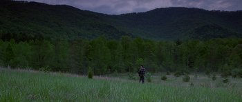 Movie still from “October Sky” (1999), directed by Joe Johnston – A man standing in a field with trees in the background; Extreme Wide shot, High angle