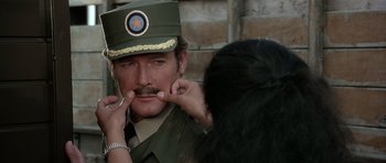 Movie still from “Octopussy” (1983), directed by John Glen – A man in a military uniform putting lipstick on a woman's face; Close Up shot, Over the shoulder angle
