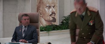 Movie still from “Octopussy” (1983), directed by John Glen – A man sitting in a chair in front of a painting; Medium shot, Over the shoulder angle