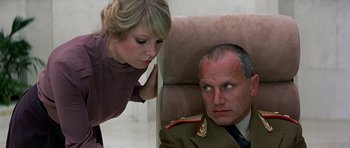 Movie still from “Octopussy” (1983), directed by John Glen – A woman standing next to a man on a chair; Medium shot, Over the shoulder angle