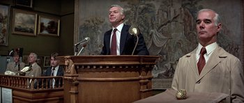 Movie still from “Octopussy” (1983), directed by John Glen – A man standing at a podium speaking to a crowd; Medium shot, Low angle