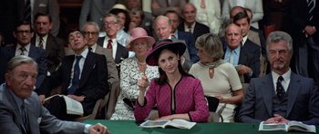 Movie still from “Octopussy” (1983), directed by John Glen – A group of people sitting around a table with a book; Medium shot, Over the shoulder angle