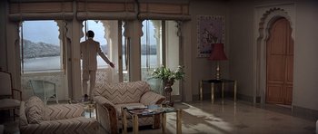 Movie still from “Octopussy” (1983), directed by John Glen – A woman standing in a living room next to an open door; Wide shot, High angle
