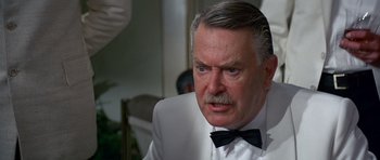 Movie still from “Octopussy” (1983), directed by John Glen – An older man wearing a white suit and a black bow tie; Close Up shot, Over the shoulder angle