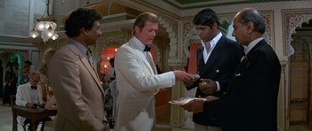 Movie still from “Octopussy” (1983), directed by John Glen – A man in a white suit is handing a piece of paper to another man in a black suit; Medium shot, Over the shoulder angle