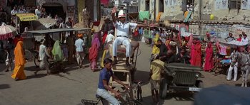 Movie still from “Octopussy” (1983), directed by John Glen – A man sitting on top of a chair on a busy street; Wide shot, High angle