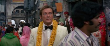 Movie still from “Octopussy” (1983), directed by John Glen – A person wearing a suit and a lei; Close Up shot, Over the shoulder angle