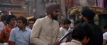 Movie still from “Octopussy” (1983), directed by John Glen – A man in a turban is holding something in his hand; Medium shot, Over the shoulder angle