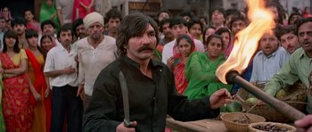 Movie still from “Octopussy” (1983), directed by John Glen – A man holding a knife in front of a group of people; Medium shot, High angle