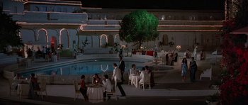 Movie still from “Octopussy” (1983), directed by John Glen – A group of people sitting around a pool at night; Extreme Wide shot, High angle